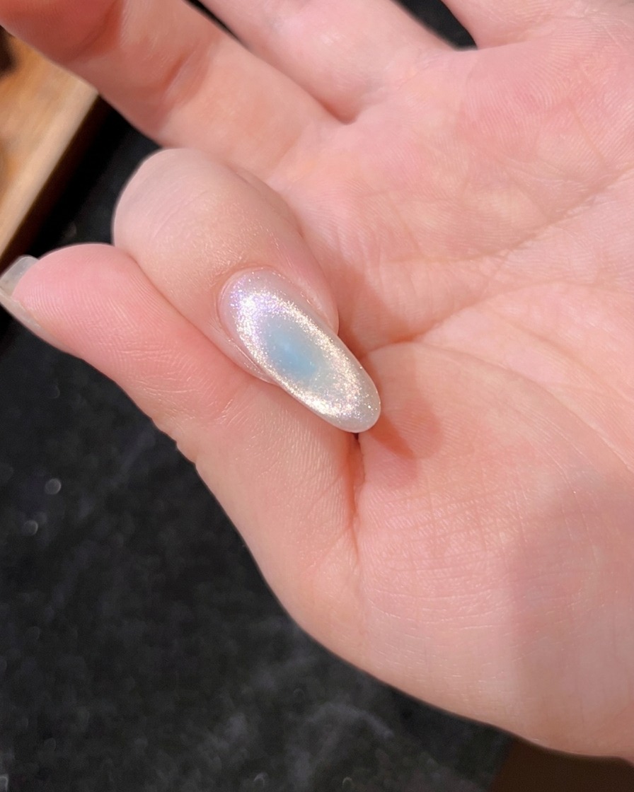 A close-up of a fingernail under the UV lamp, showing the blue gel being cured.