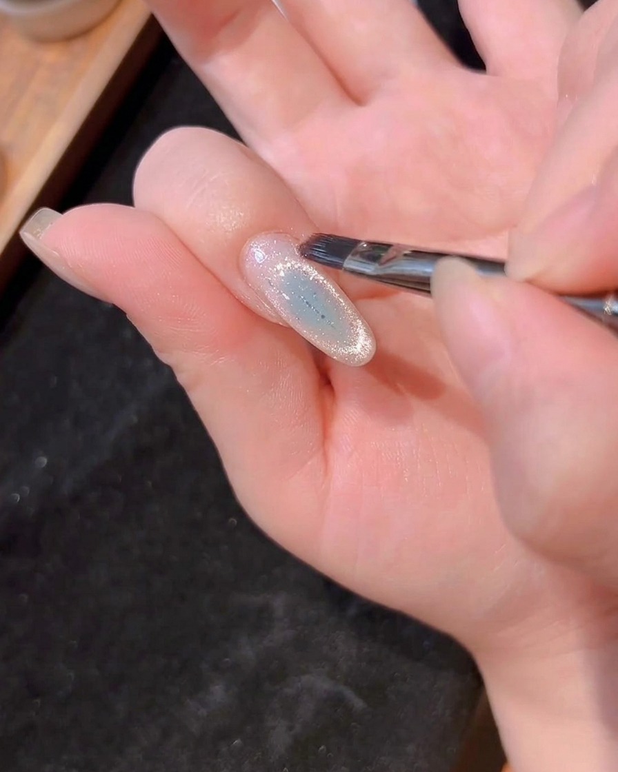 A nail brush applying a thin, clear layer of builder gel over the nail.