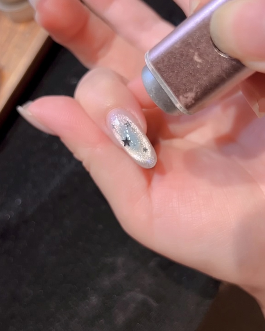 A handheld UV lamp curing the nail decorated with silver lines and star glitters.