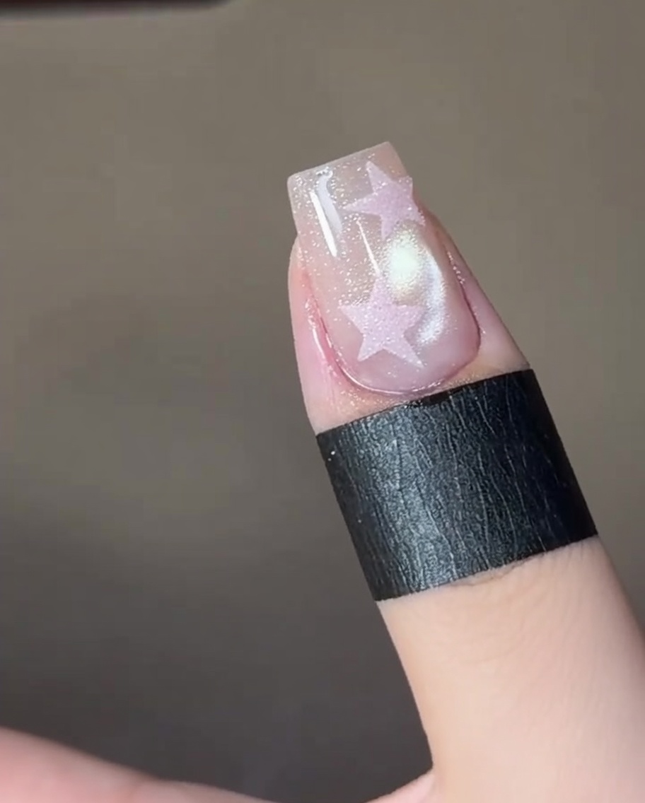 Tweezers placing a star stencil sticker onto a manicured fingernail.