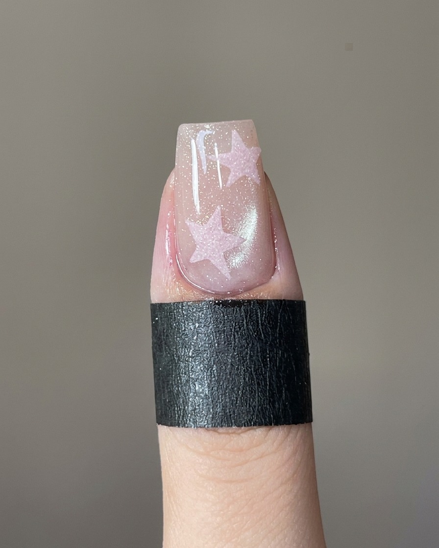 A fine-detail nail brush filling in a star stencil on a fingernail with pink gel.