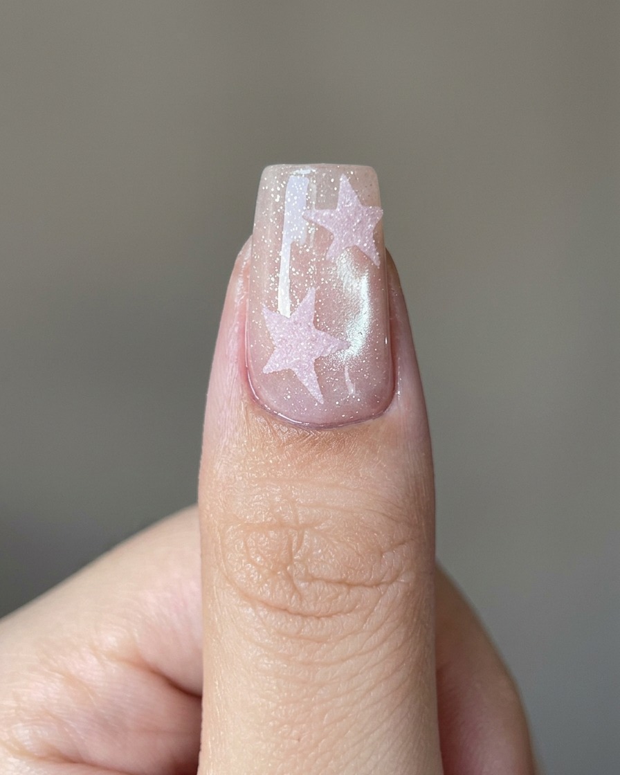 A brush applying a clear top coat layer over a pink star design on a nail.