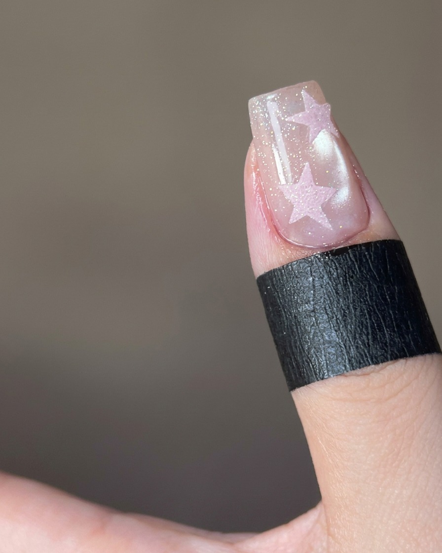 A close-up showing pink sugar powder being sprinkled onto a star-shaped design on a nail.