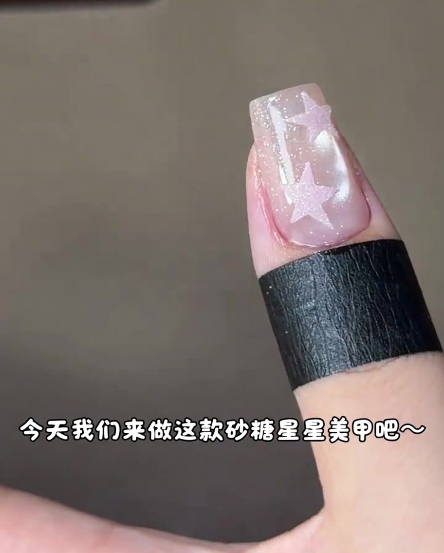 A fingernail with a pink star design being cured under a UV nail lamp.
