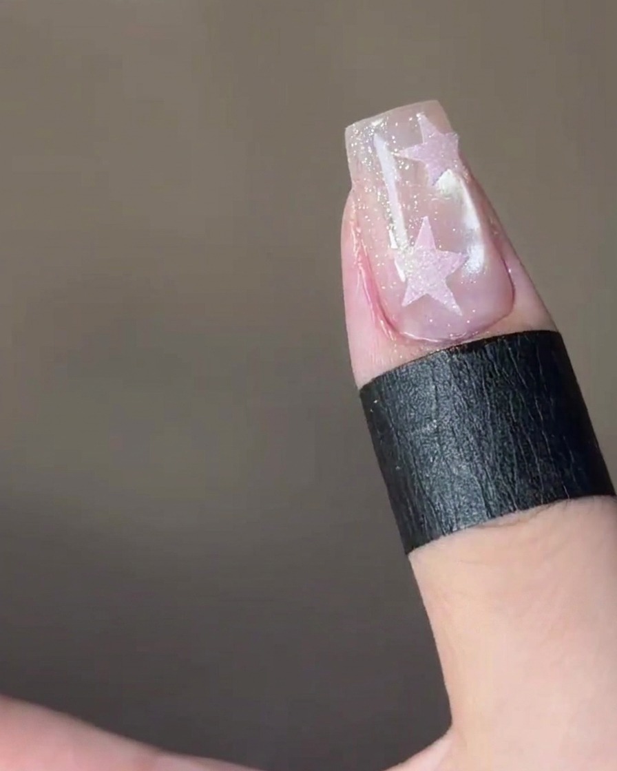 A star-shaped sticker being placed onto the tip of a fingernail.