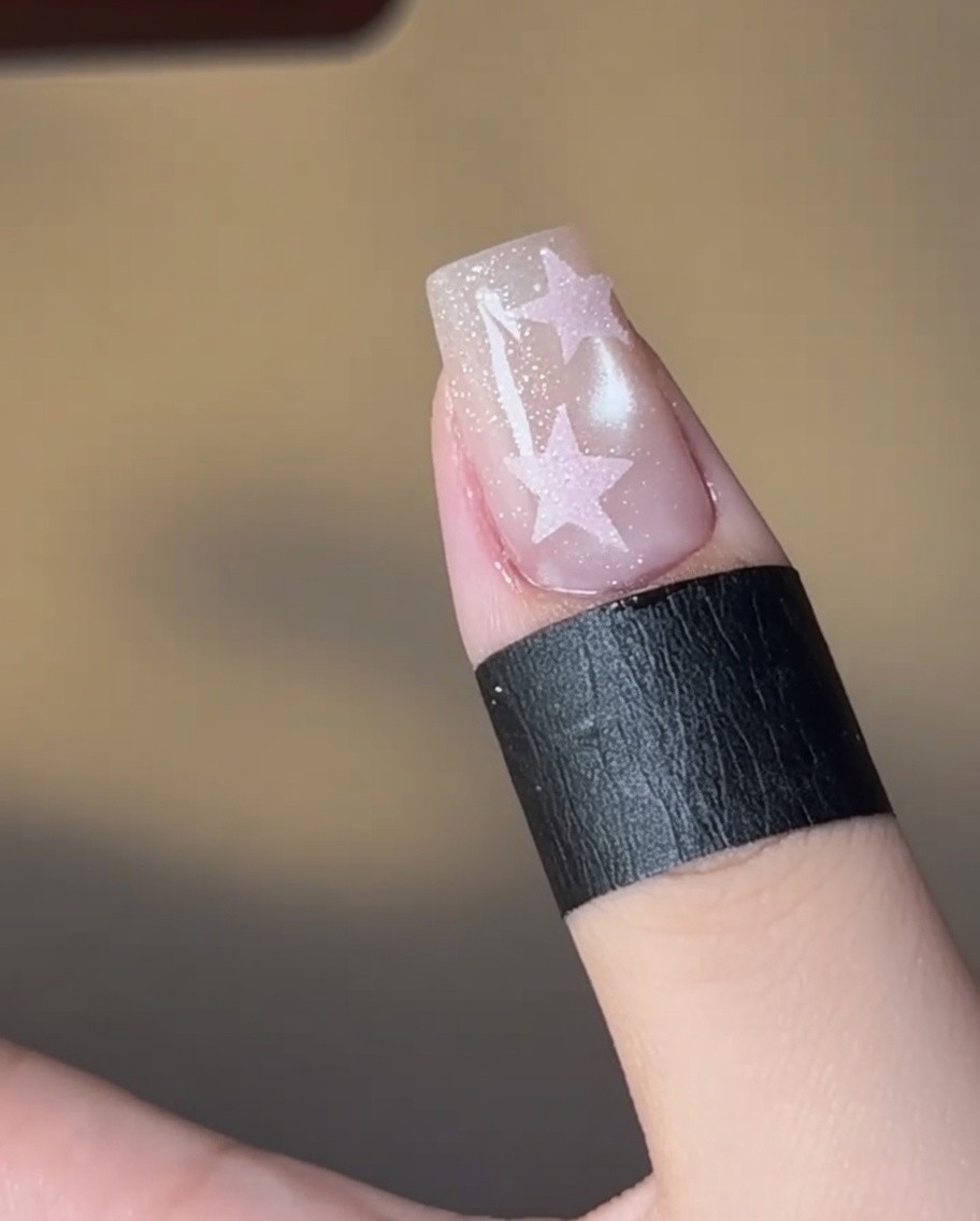 A nail with a pink-filled star design curing under a lamp.