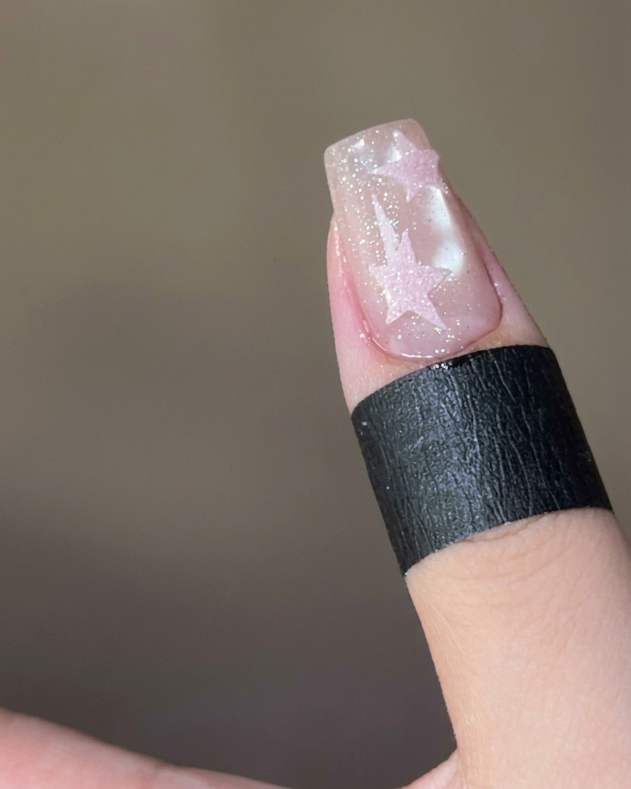 Pink sugar powder being sprinkled onto a wet top-coat covered star on a nail.