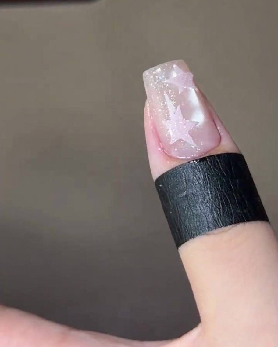 A finished nail with two textured pink sugar stars, curing inside a UV nail lamp.