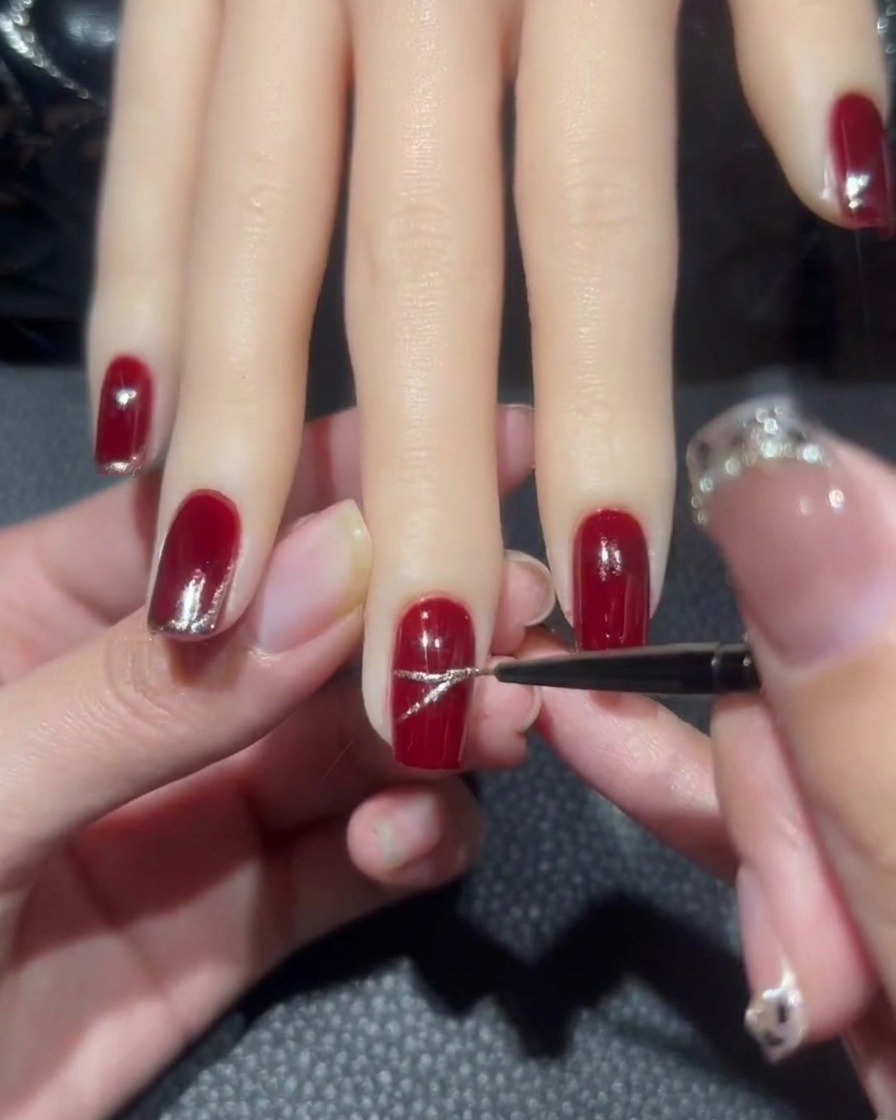 A detailed shot showing a rose-gold glitter X being drawn on the center of a manicured red nail.