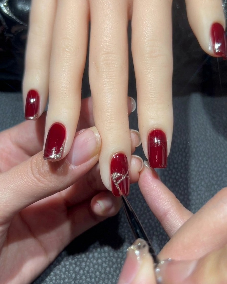 A close-up of the middle finger nail showing the X shape being filled in with dense rose-gold glitter to resemble a bow.