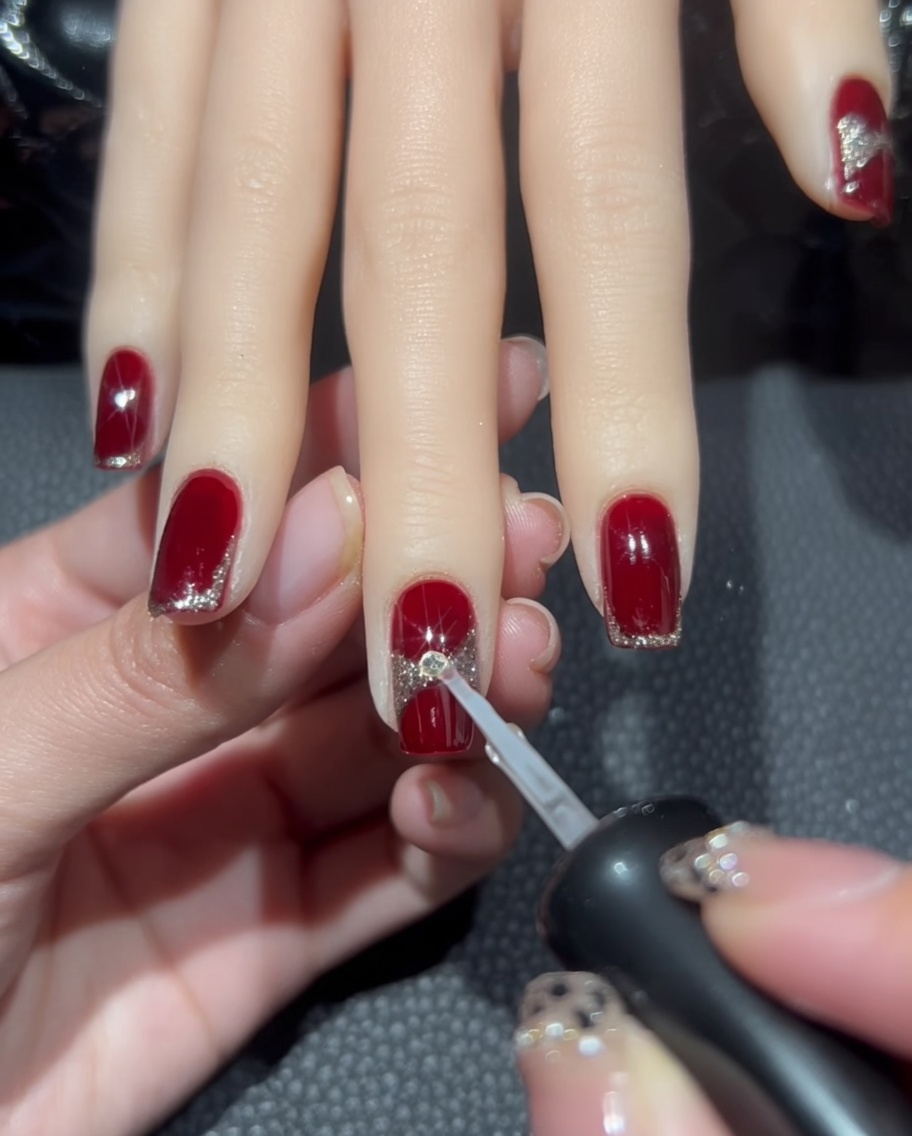 A drop of clear nail glue being placed at the center of the glitter ribbon design on the nail.