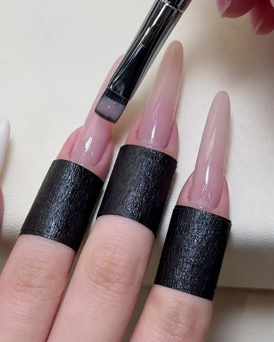 Close-up view of a brush applying a sheer nude gel polish over the entire nail plate.