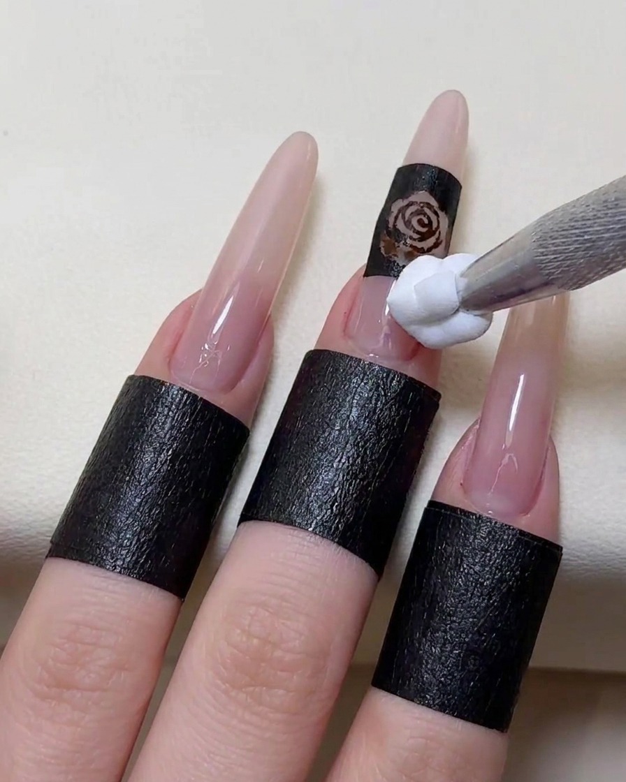 A sponge-tipped applicator dabbing white gel polish over a stencil placed on a fingernail.