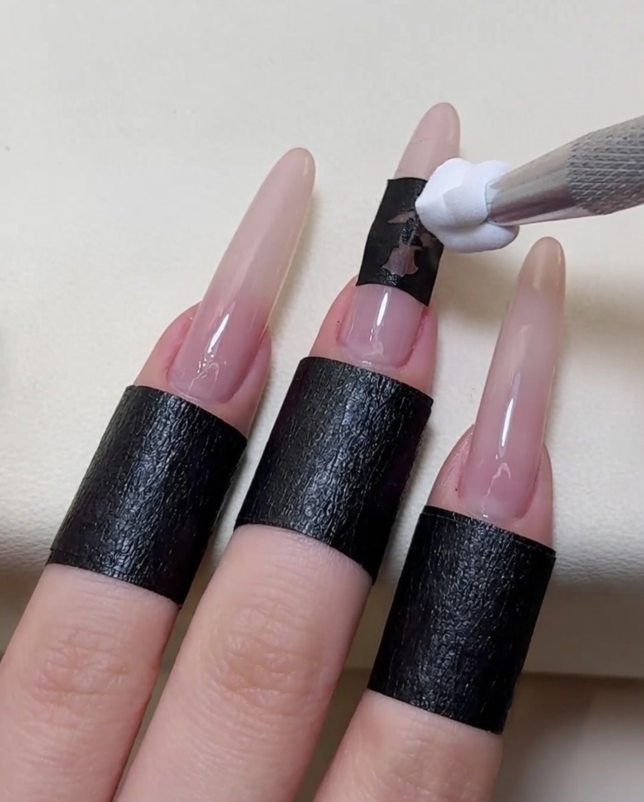 The stencil sticker being carefully lifted off the nail, revealing a crisp white rose design underneath.