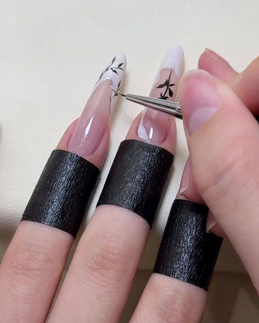 A nail brush applying a metallic silver highlight along the edge of the painted branch design.