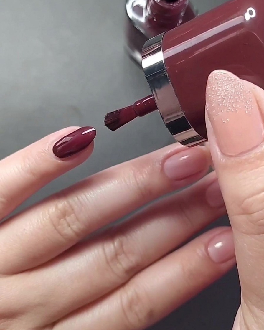 A close-up view of applying a light nude beige nail polish to the ring fingernail.