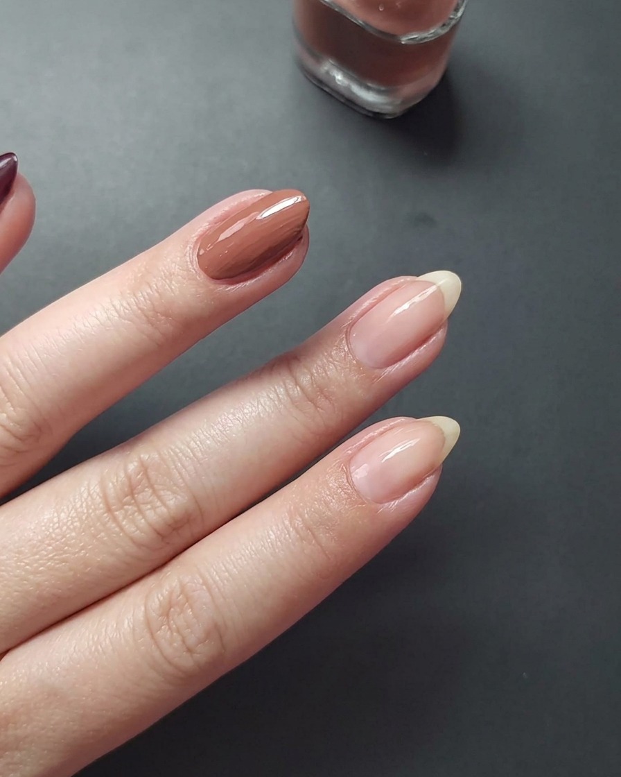 A close-up view showing the application of mauve colored nail polish onto the middle fingernail.