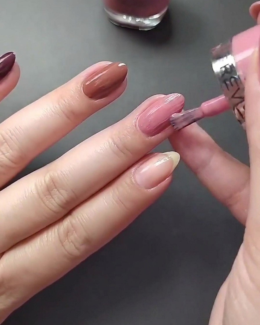 A close-up view of applying light nude nail polish to the thumbnail.