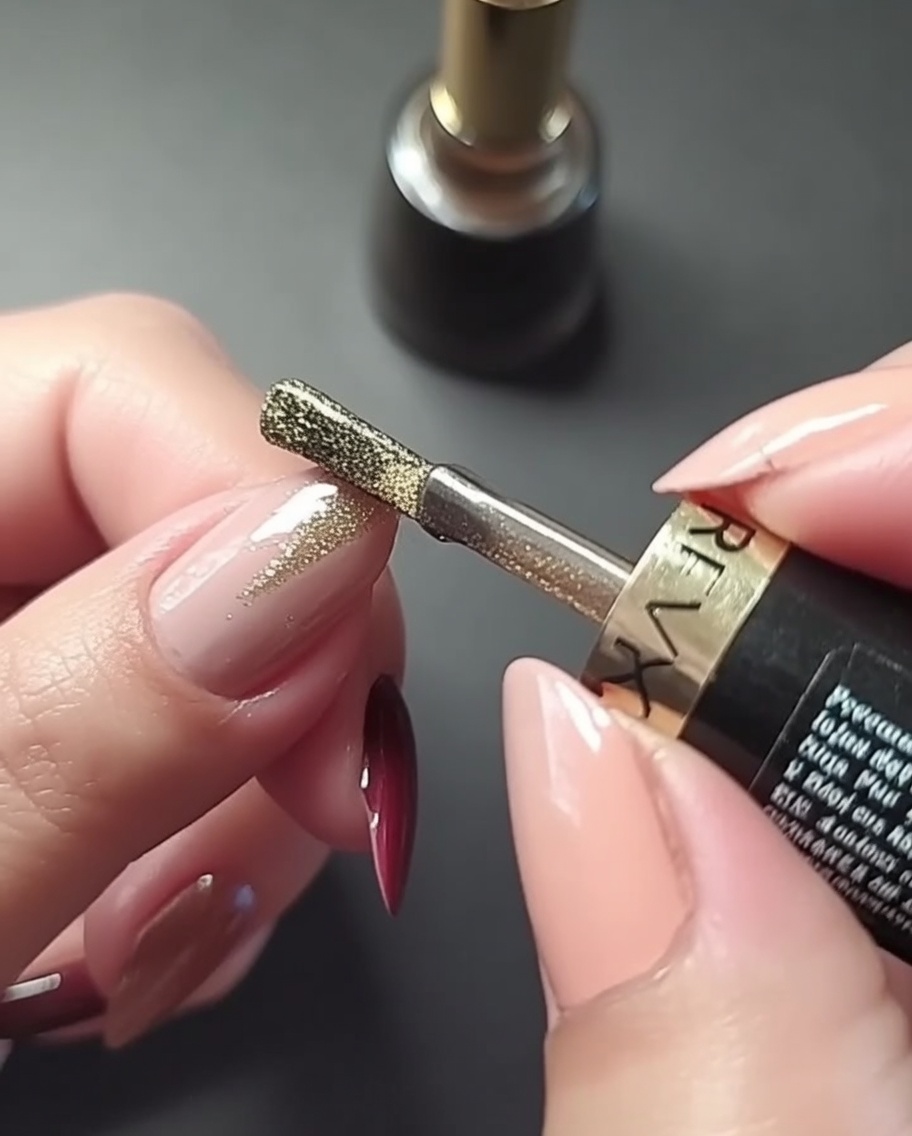A close-up view of a hand painting a precise vertical gold line down the center of a rose pink manicured fingernail.