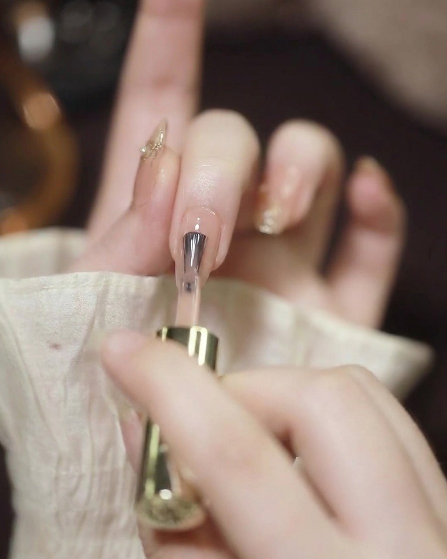 Close-up of a nail brush applying a sheer nude gel polish to a prepared, clean fingernail.