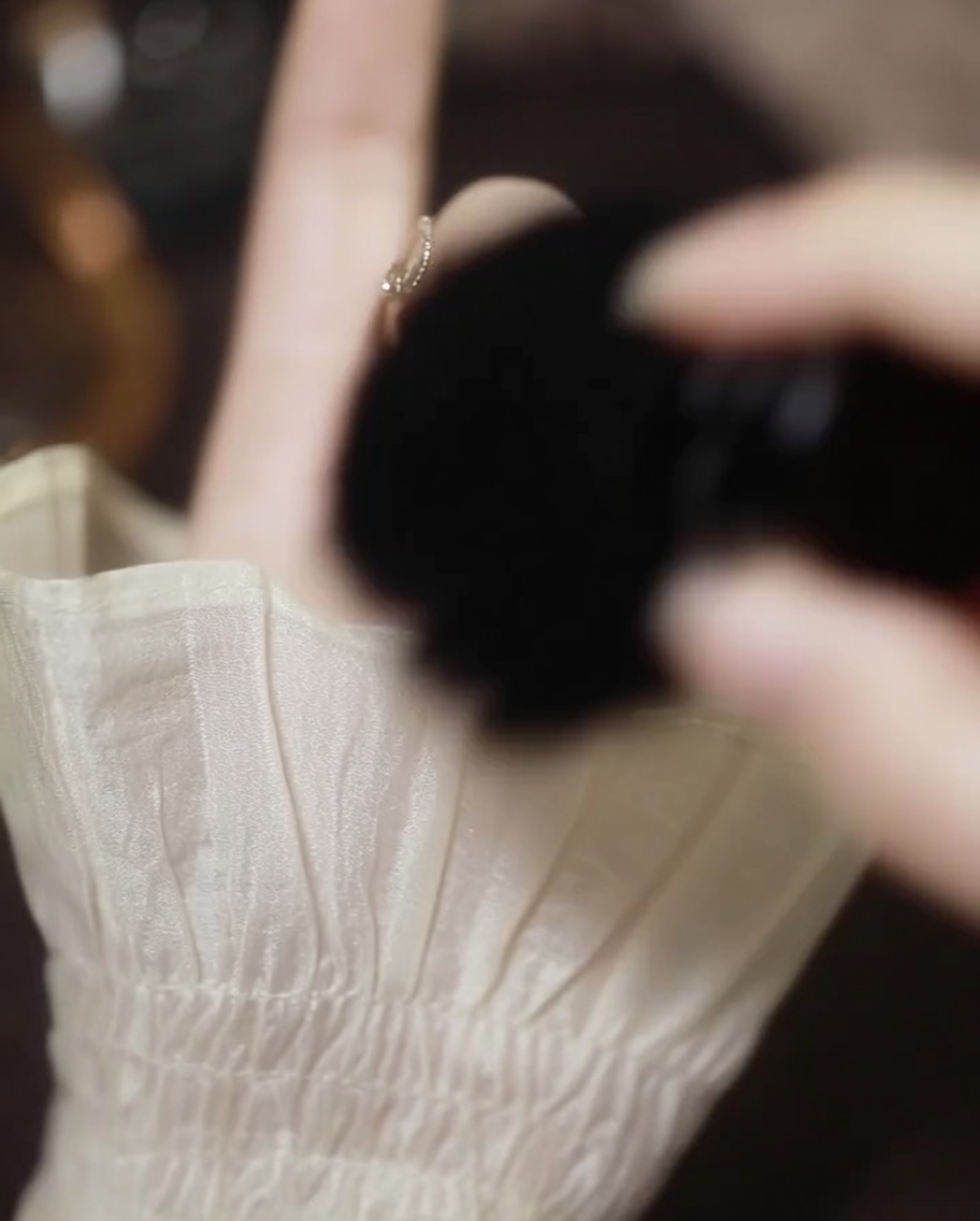 A soft black brush sweeping excess rose gold powder off the nail and finger.