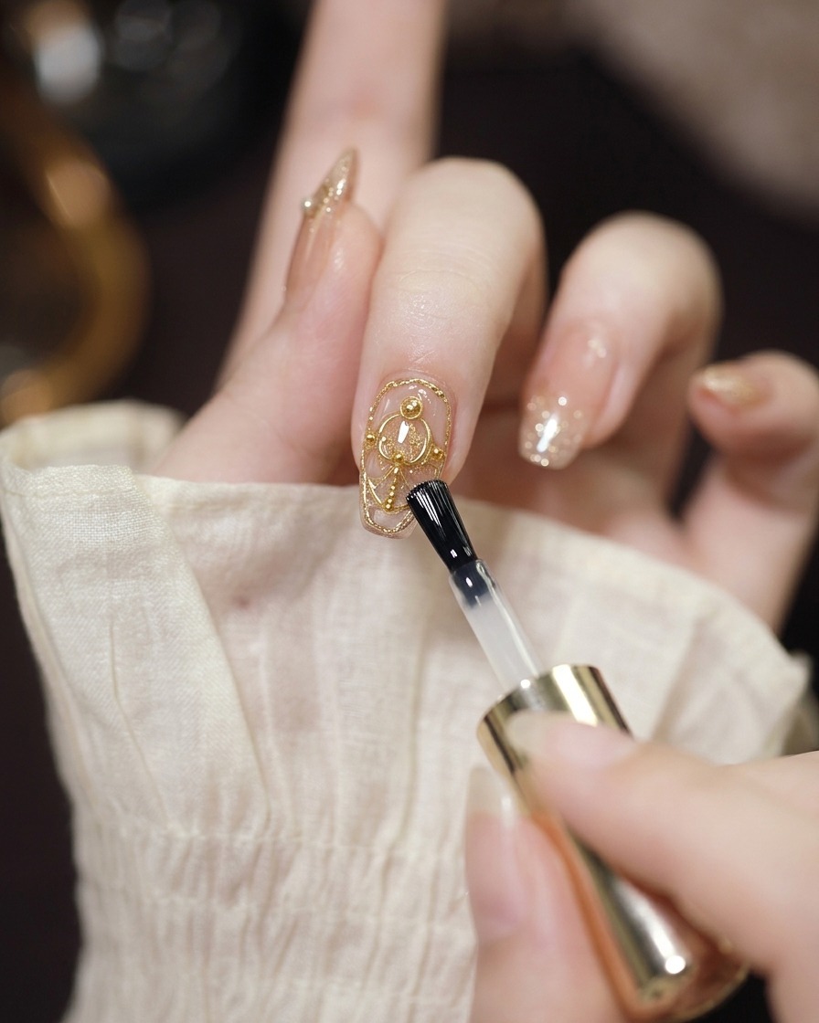 A clear gel brush applying a protective layer over a nail decorated with chrome and pearls.
