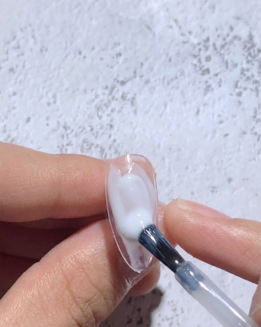 A fine brush blending wet white gel on a nail tip to create a soft-focus center.
