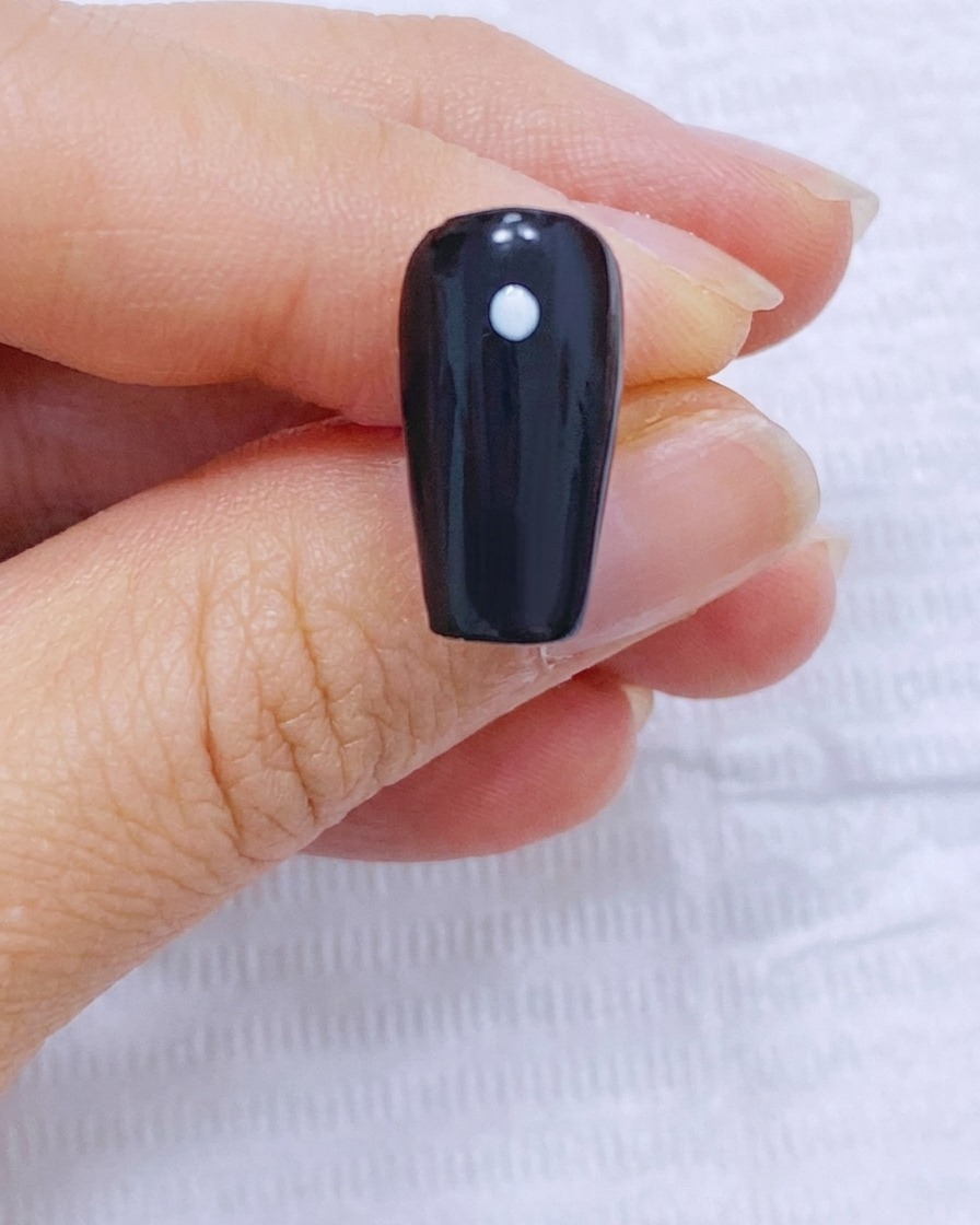 A black nail with one white center dot and four peripheral dots arranged in a circle.