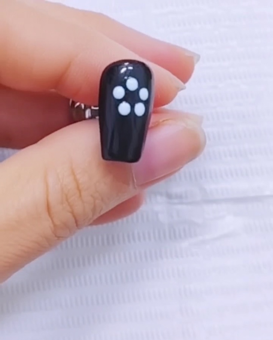 A fine liner brush dragging white gel outward from the center of the flower design on a black nail.
