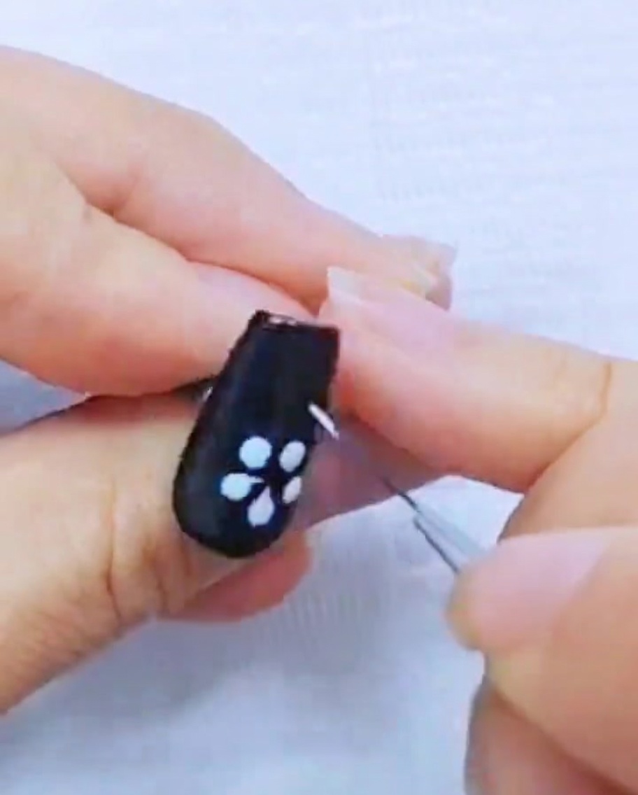 Close-up of a liner brush refining the white gel petals on a black nail.