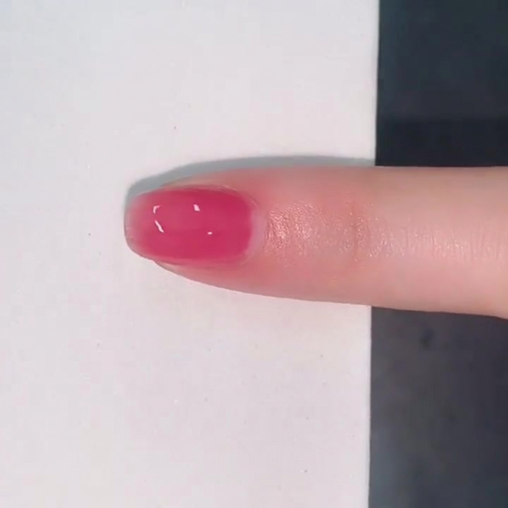 A single fingernail coated in a glossy translucent layer of pink jelly polish.