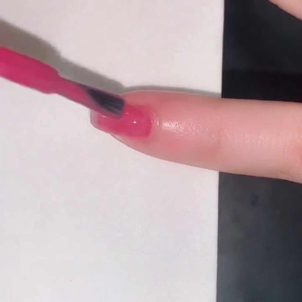 A nail polish brush adding a third layer of pink jelly gel to build color intensity on the fingernail.