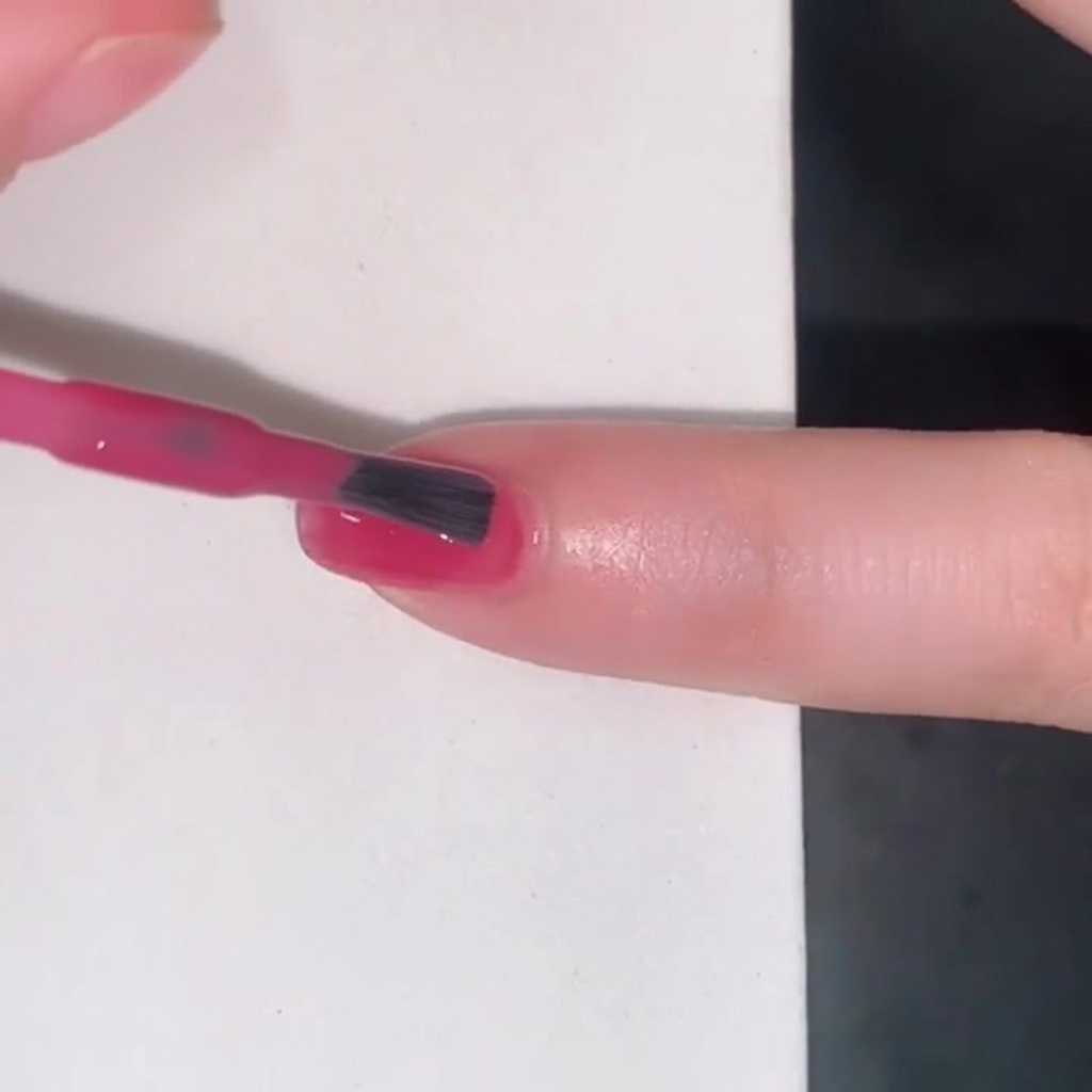 A brush applying a translucent pink jelly polish onto a fingernail.