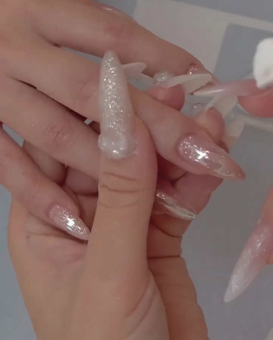 A close-up view showing a brush applying a sheer, jelly-like gel base coat to a natural nail.