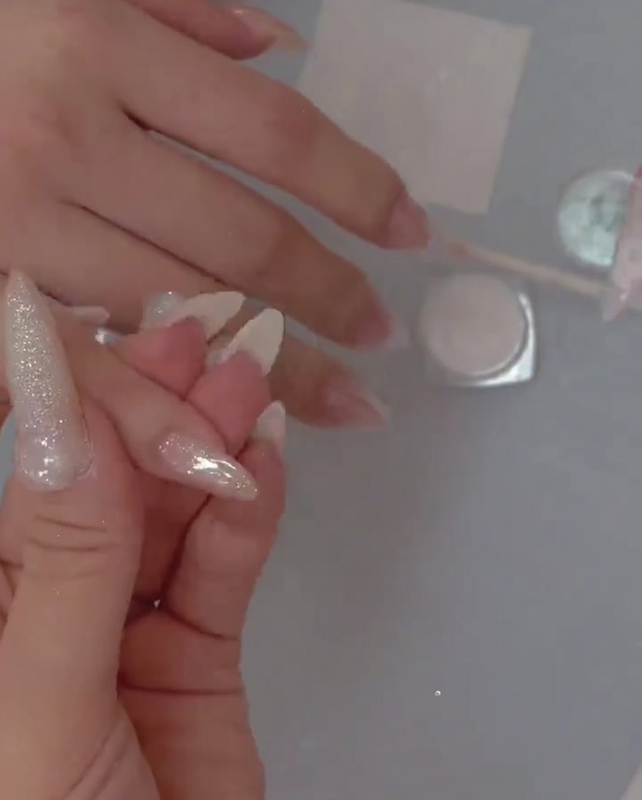 A detail brush carefully placing fine glitter polish over the base coat on the nail.