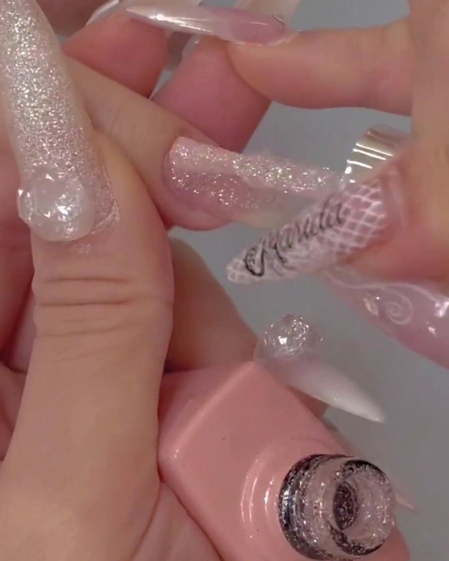 The tip of a gel bottle brush applying a smooth, clear top coat over a textured glitter nail.