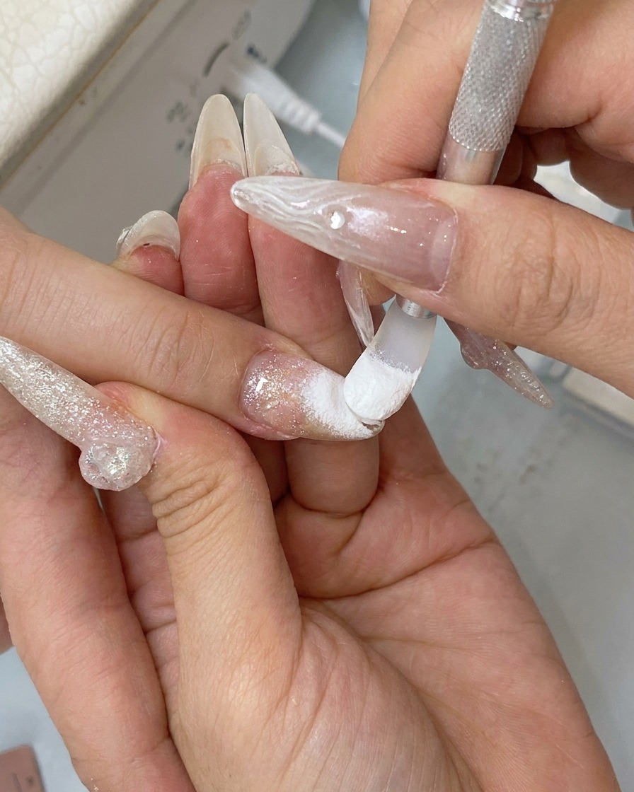 A finger rubbing the surface of a nail to buff the chrome powder into a reflective mirror finish.