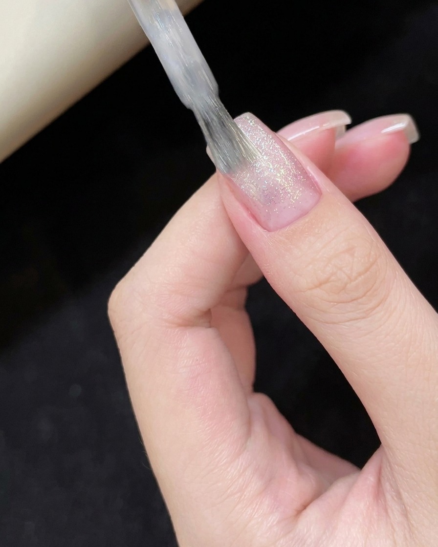 Applying sheer white cat-eye polish to the nail surface.