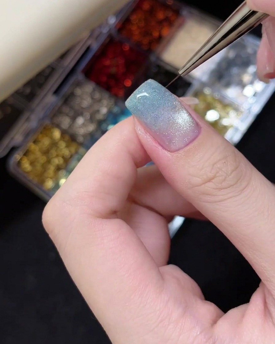 Tweezers placing a small silver star glitter charm onto the tip of a manicured nail.