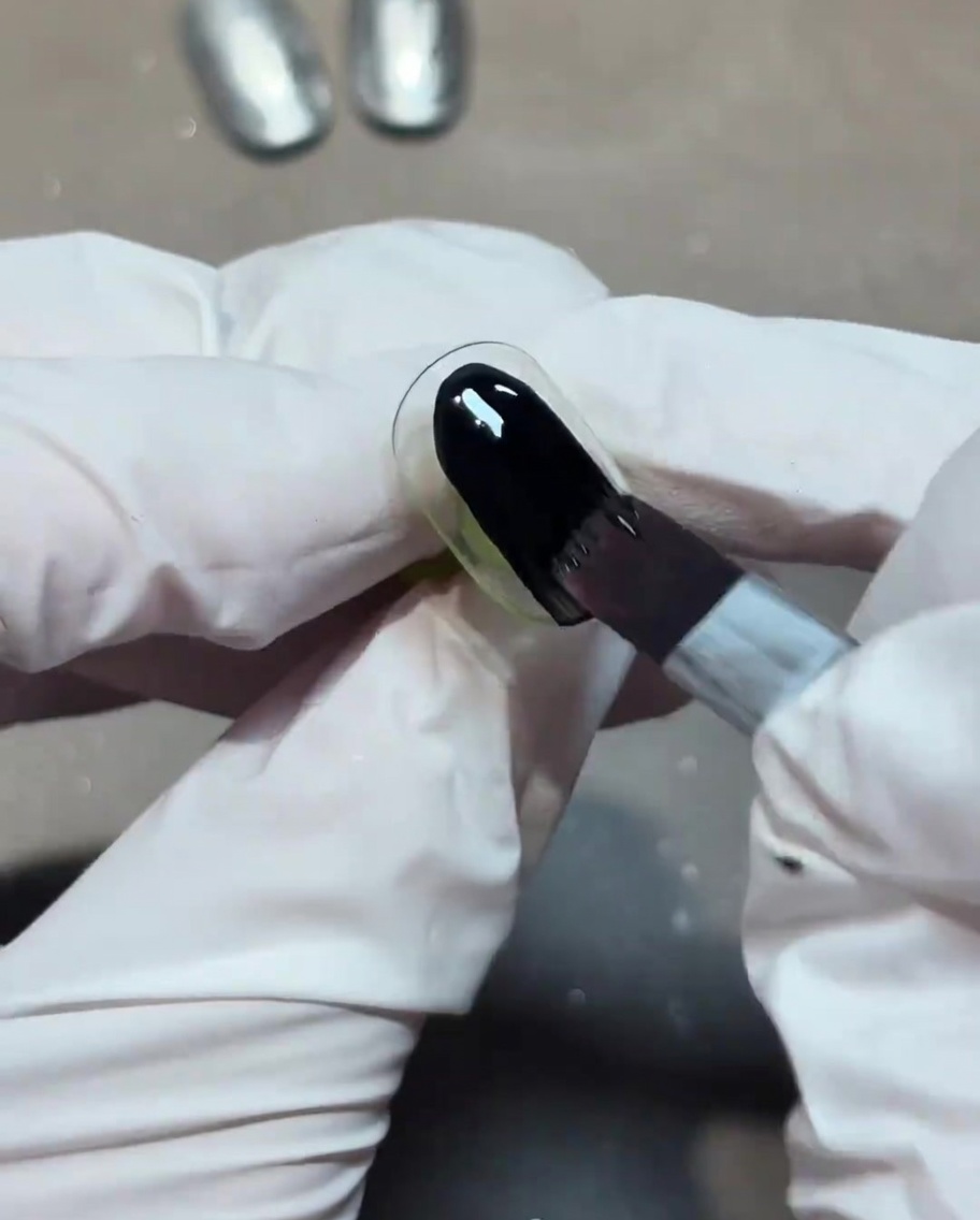 A brush applying a coat of opaque black gel polish to a nail.