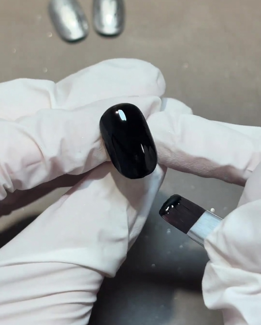 Applying a clear, shiny top coat over a black nail base.