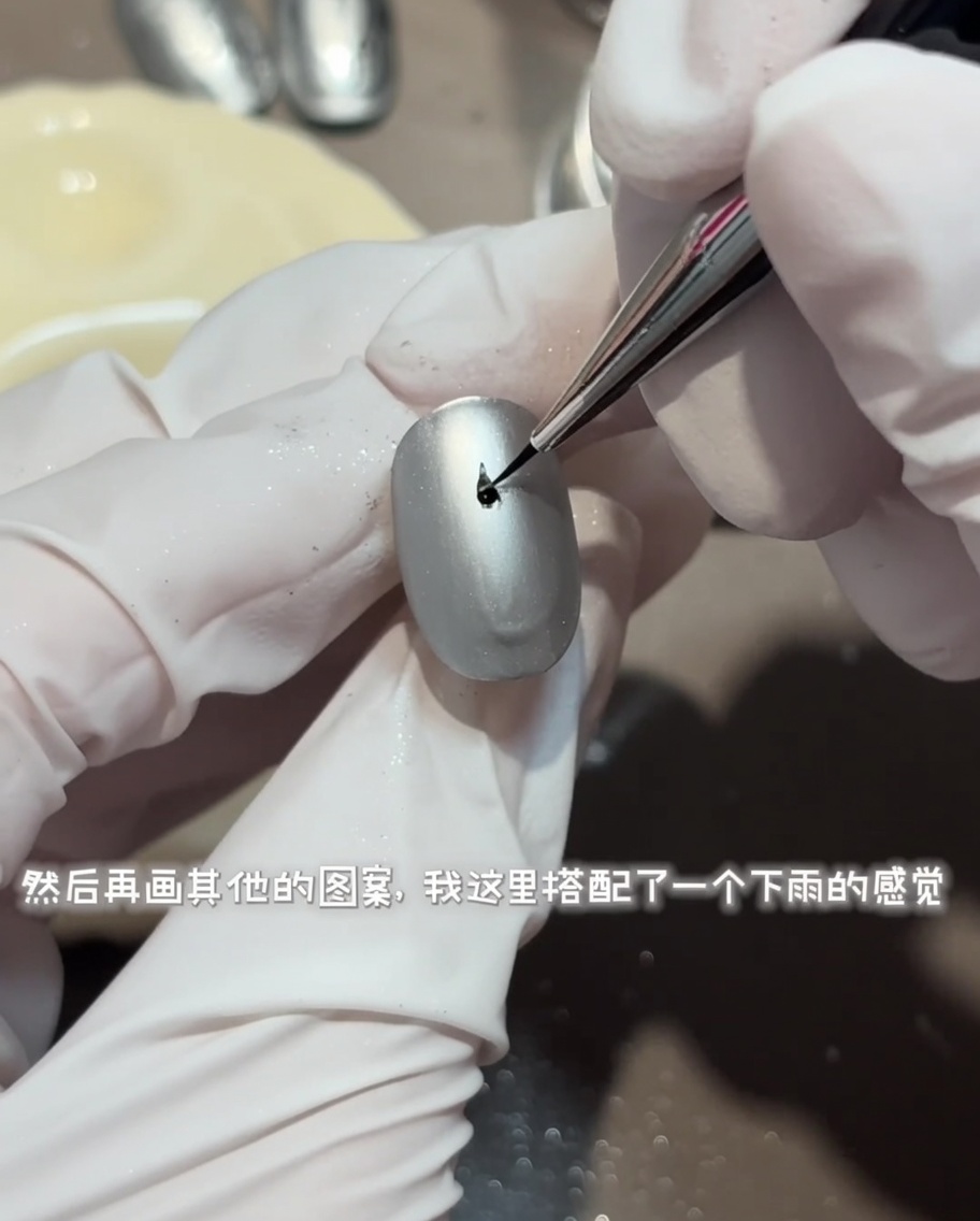 A fine liner brush drawing a detailed, circular water ripple design with shiny top coat on a matte gray nail.