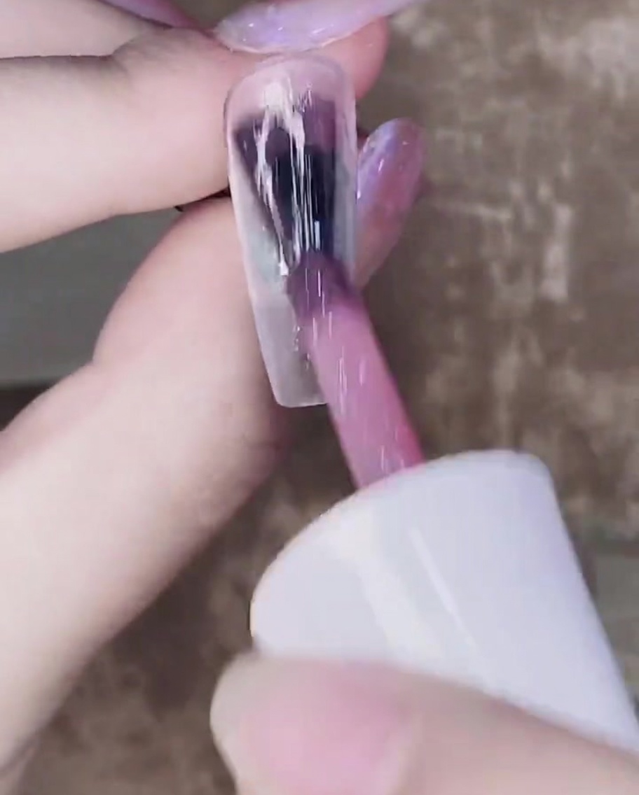 A brush applying a second coat of sheer pink gel over the first cured layer.