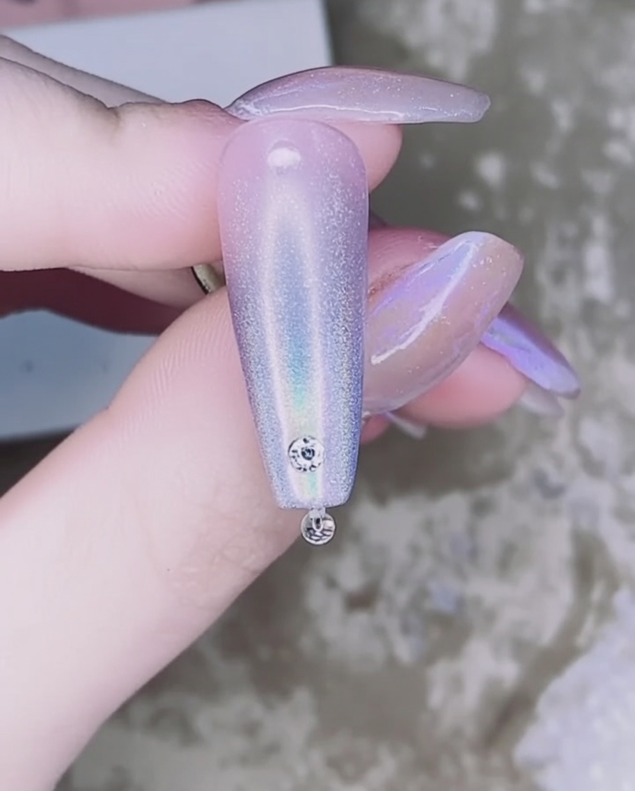 Tweezers holding a small, clear rhinestone and placing it onto the adhesive drop on the nail.