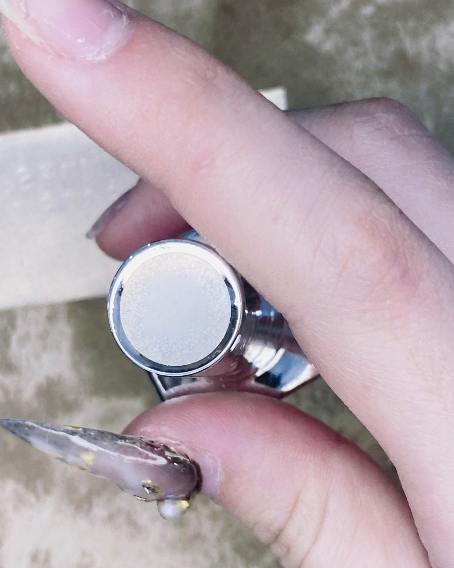 A thin nail art brush applying a small bead of top coat around the base of a rhinestone mounted on a nail.