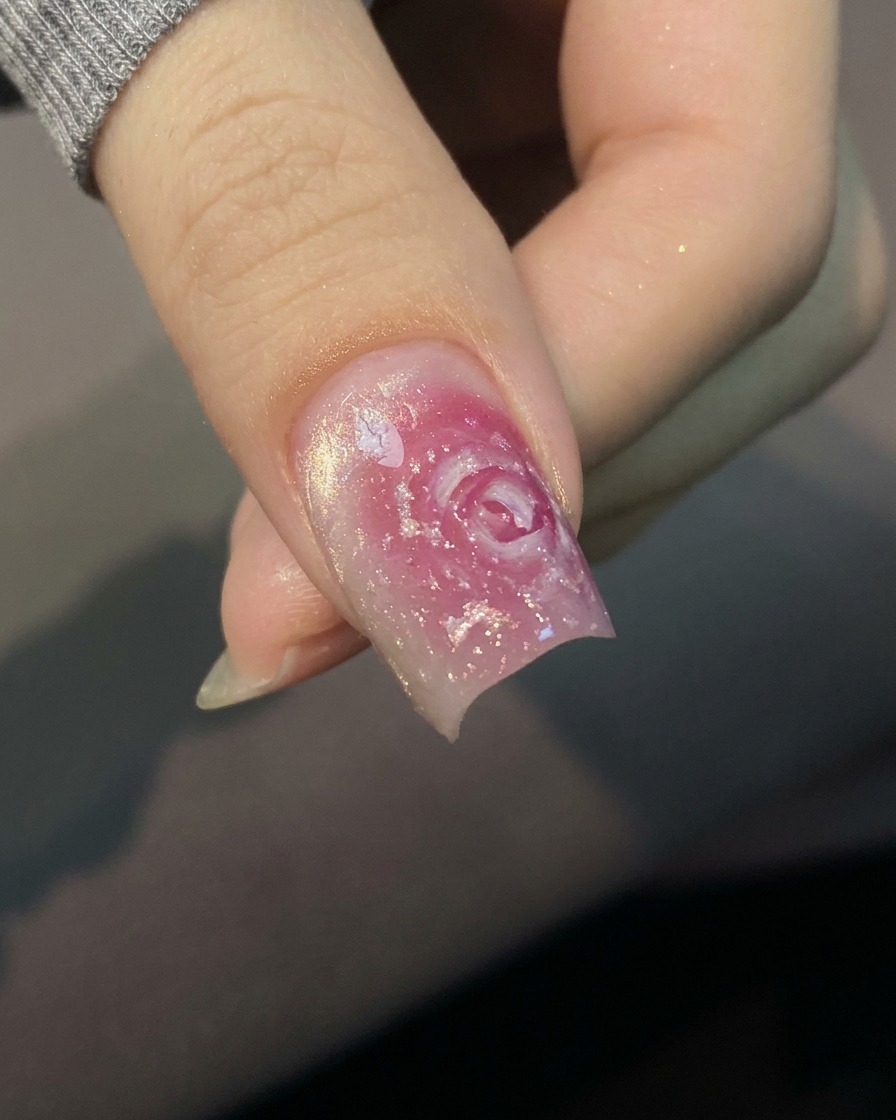 A close-up view of a brush applying a clear base coat to a natural, unpainted fingernail.