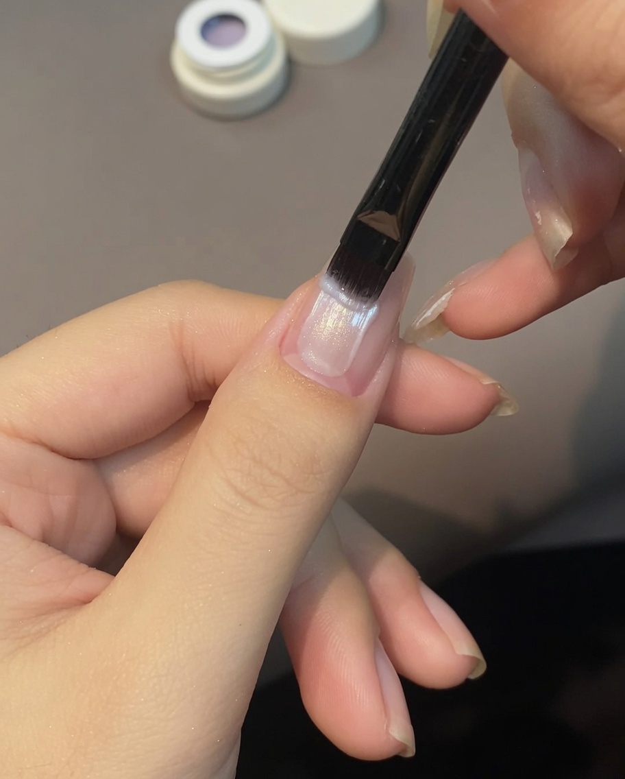 A brush applying light purple cat eye gel across a fingernail.