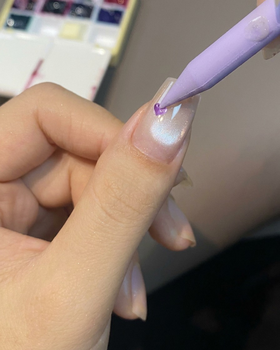 A pointed tool placing a small drop of translucent gel onto the center of a prepped cat eye nail.