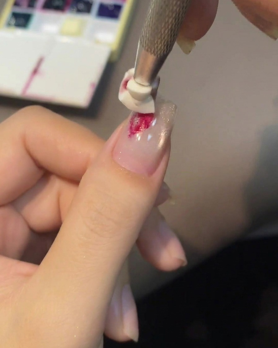 A silicone embossing tool pressing into a drop of red gel on the nail to create a blooming rose center.