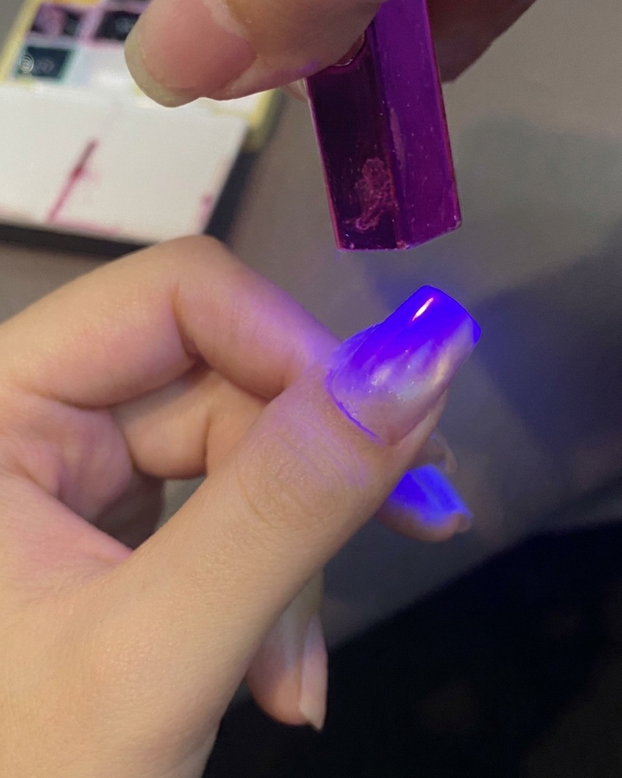 A fingernail being cured under a purple mini UV light to set a gel design.
